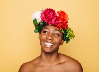 Mulher sorrindo e utilizando uma coroa de flores multicoloridas na cabeça.