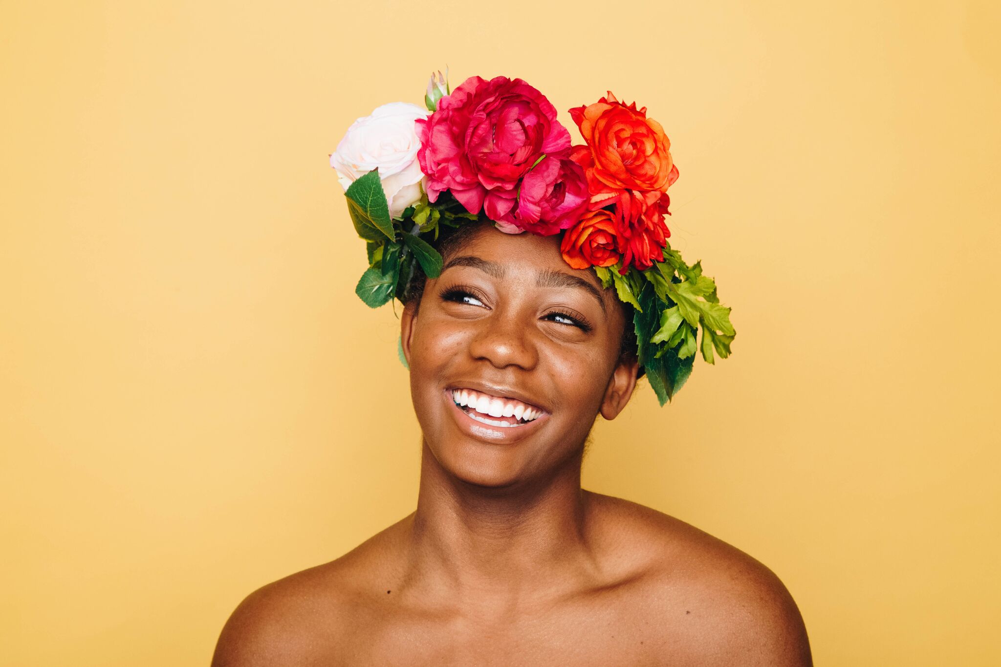 Mulher sorrindo e utilizando uma coroa de flores multicoloridas na cabeça.